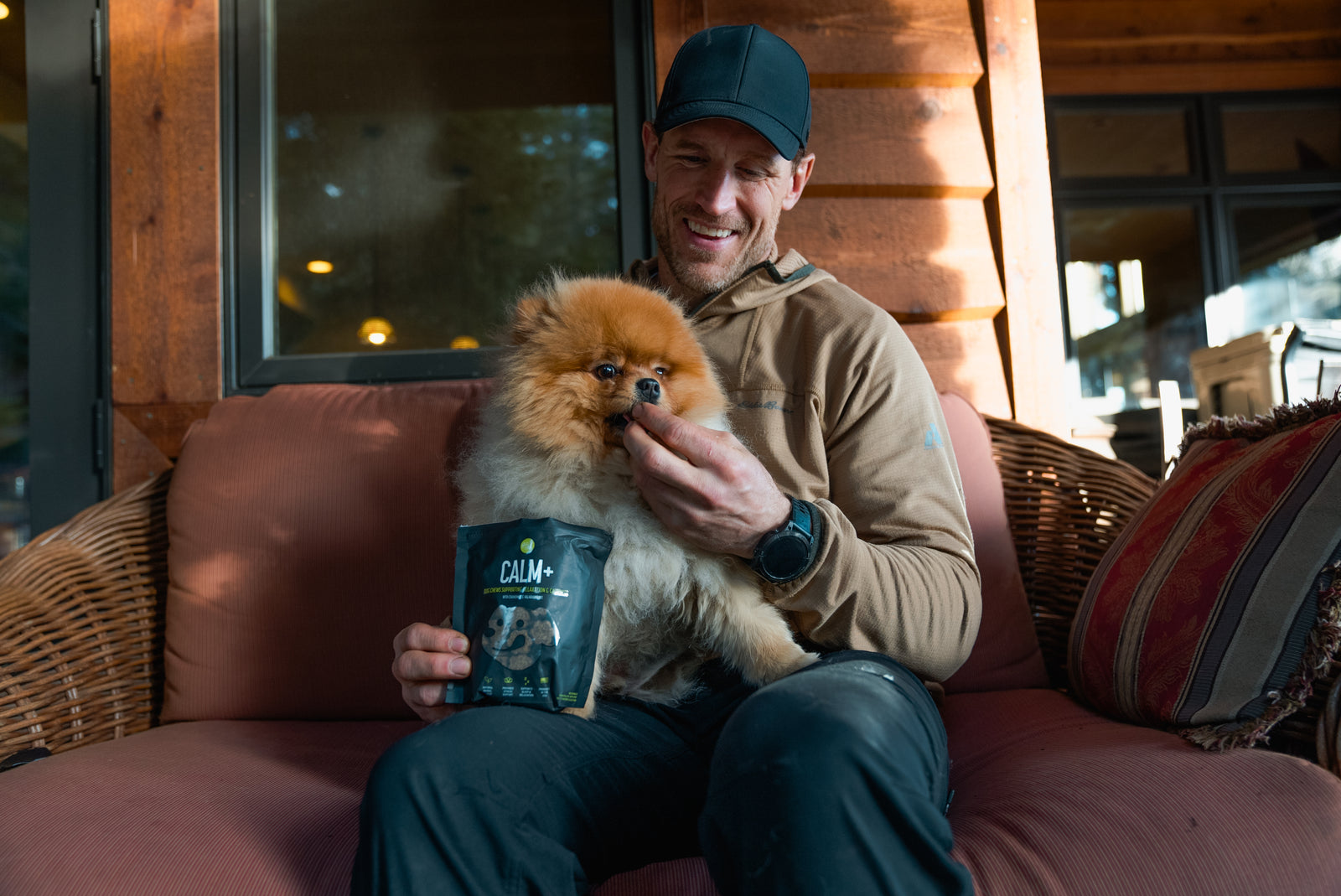 A woman sits in bed with her dog and cuddles under blankets. A black bag of Calm+ supplements is displayed.