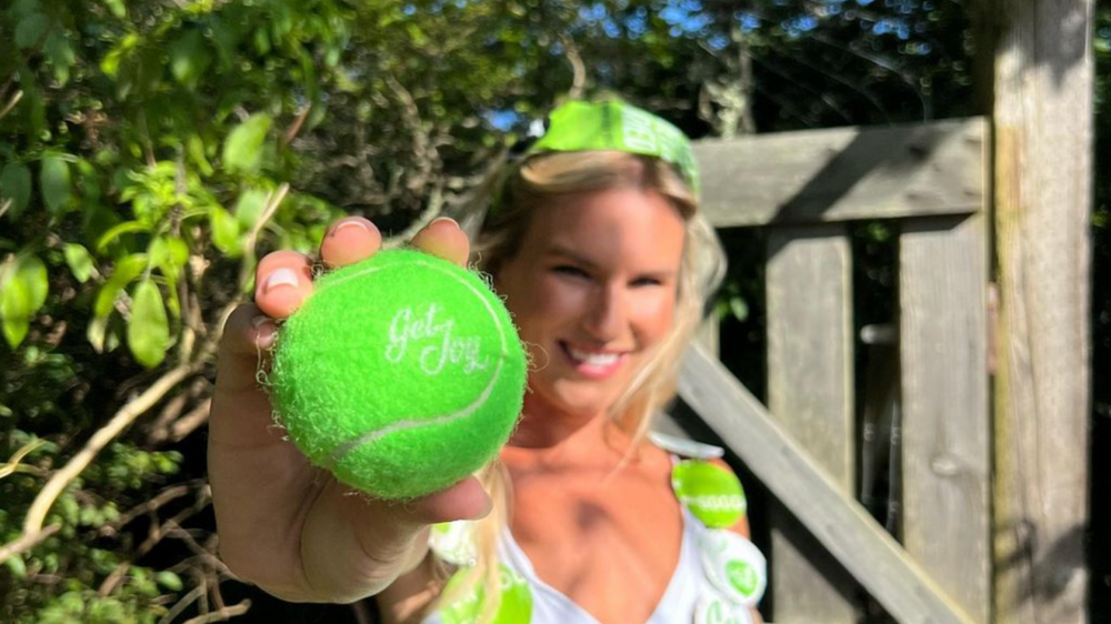 A woman holds a green tennis ball with a Get Joy label.