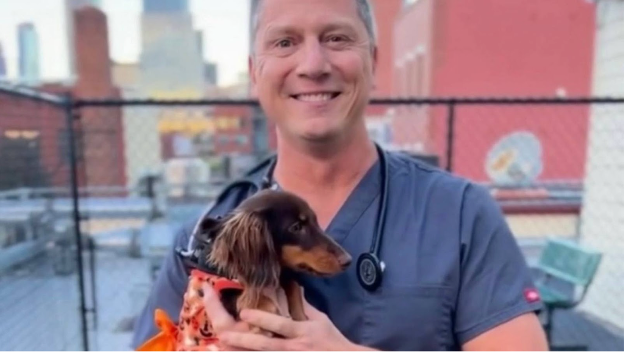 A Get Joy vet holds a small brown dog outside and smiles.