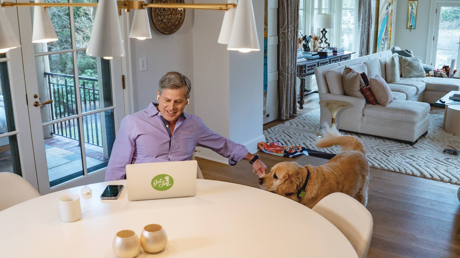 A man sits at his table on his laptop as his golden retriever stands by his side.