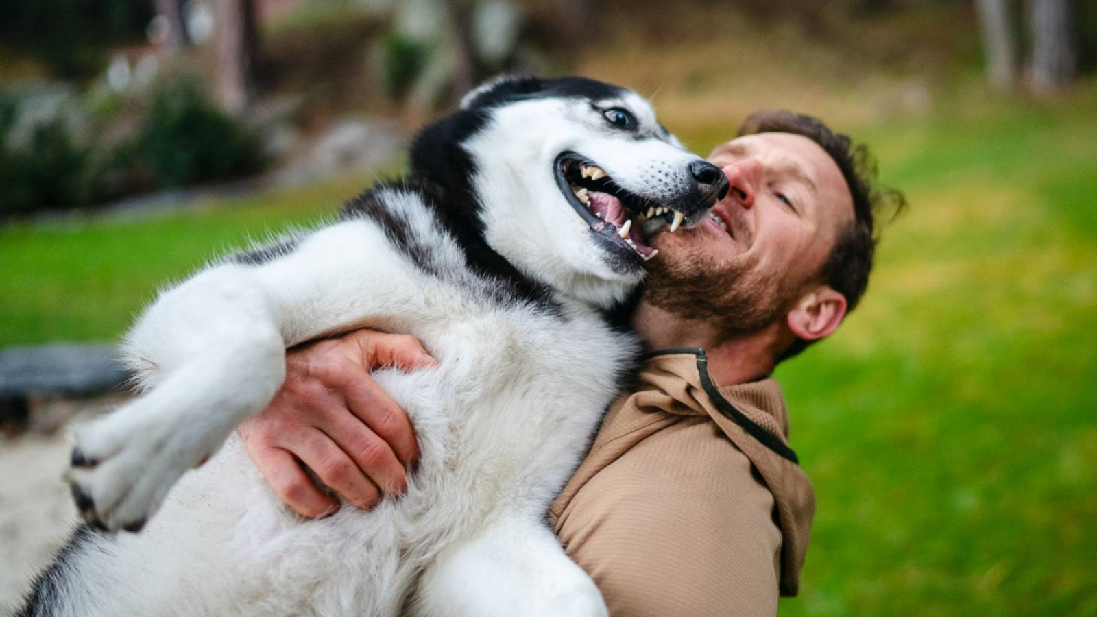 A man holds his Husky dog in his arms and smiles.