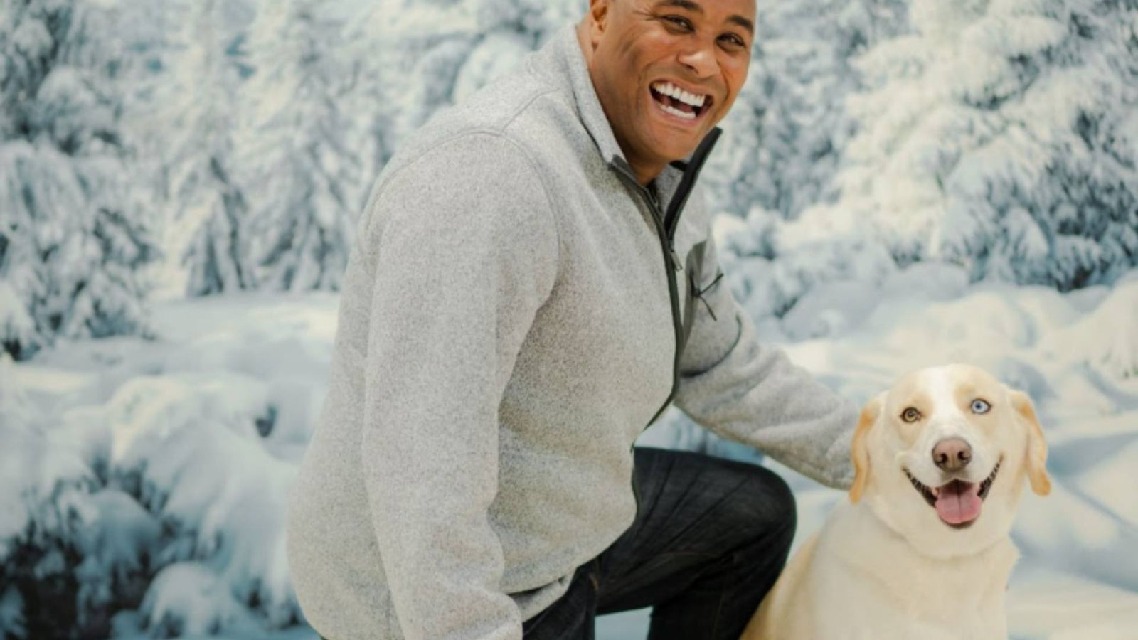 A man and his dog pose happily in front of a winter wonderland screen.