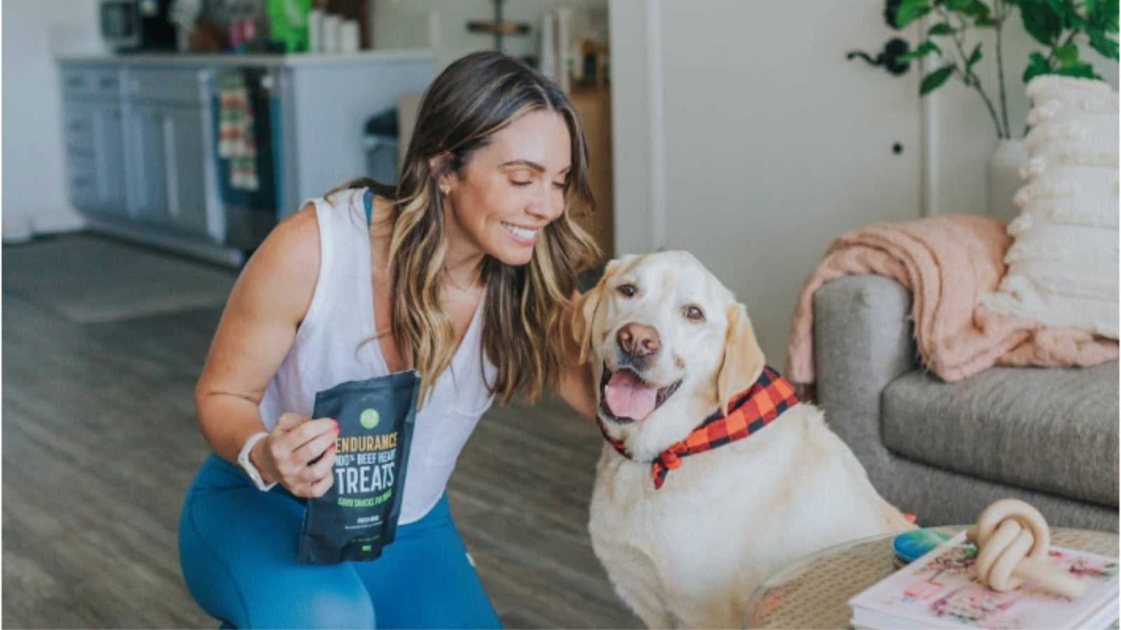 A woman sits with her dog and holds Get Joy treats, demonstrating a post-grooming experience.