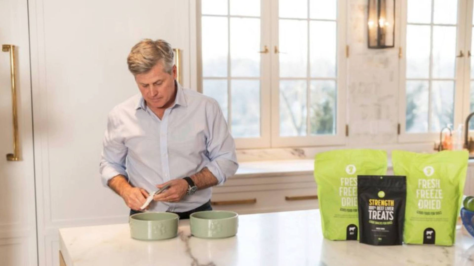 A man stands at his kitchen counter and prepares two dog bowls of delicious Get Joy dog food.