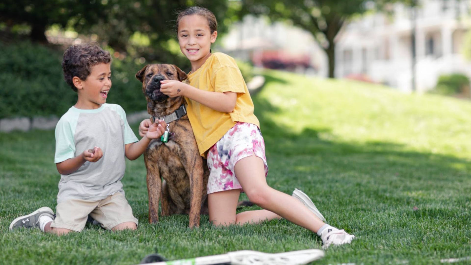 Two smiling kids sit outside on the grass with their puppy sitting between them.